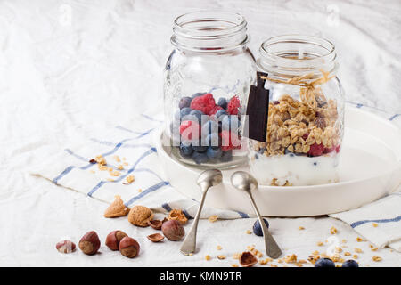 Glas mit hausgemachtem Müsli und Joghurt serviert mit Nüssen, Himbeeren und Brombeeren über weiße Textil Stockfoto