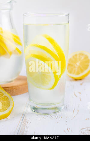 Ein Becherglas und einen Krug kalten Limonade auf einem weißen Hintergrund Holz umgeben von Zitronen Stockfoto