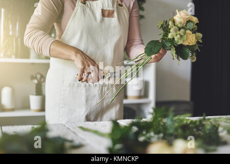 Junge Frau, die an einem Tisch in Ihrem Blumenladen trimmen die Stiele der Blumen und einen Blumenstrauß Stockfoto