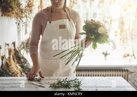 Junge Frau, die an einem Tisch in Ihrem Blumenladen trimmen die Stiele der Blumen und einen Blumenstrauß Stockfoto