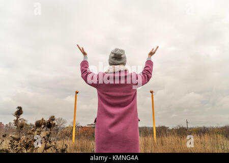 Frau in Mäntel und Hüte steht mit ihrem hands up, betet für gutes Wetter, eine Rückansicht Stockfoto