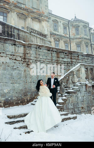 Vewrical in voller Länge des charmanten Fröhliche jungvermählte Paar stehend auf dem starsif des alten Gebäudes mit Schnee bedeckt. Stockfoto