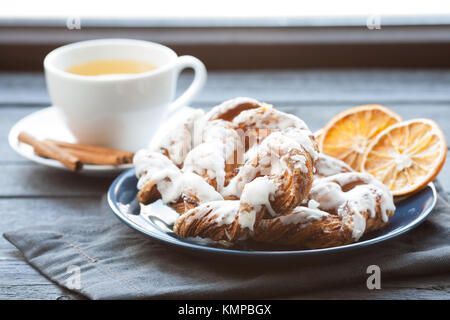 Bayerische Creme puff mit zerquetschten Haselnuss und Zitrone Fondant auf einem blauen Schild. Im Hintergrund, grüner Tee mit Zimtstangen. Stockfoto