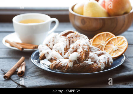 Bayerische Creme puff mit zerquetschten Haselnuss und Zitrone Fondant auf einem blauen Schild. Im Hintergrund, grüner Tee mit Zimtstangen und eine hölzerne Schüssel mit Stockfoto