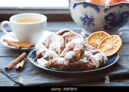 Bayerische Creme puff mit zerquetschten Haselnuss und Zitrone Fondant auf einem blauen Schild. Im Hintergrund, grüner Tee mit zimtstangen und ein Glas Vase. Stockfoto