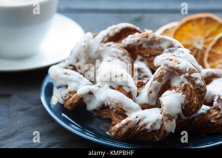 Bayerische Creme puff mit zerquetschten Haselnuss und Zitrone Fondant auf einem blauen Schild. Im Hintergrund eine Tasse Tee und Scheiben getrocknete Orangen. Stockfoto