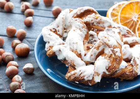 Bayerische Creme puff mit zerquetschten Haselnuss und Zitrone Fondant auf einem blauen Schild. Im Hintergrund eine Tasse Tee und Scheiben getrocknete Orangen. Stockfoto