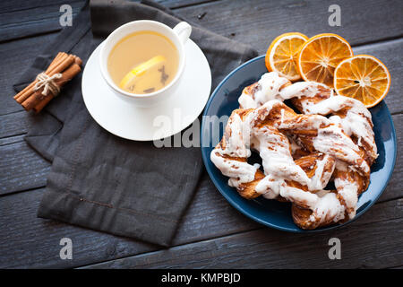 Bayerische Creme puff mit zerquetschten Haselnuss und Zitrone Fondant auf einem blauen Schild. Im Hintergrund, grüner Tee mit Zitrone und Zimtstangen. Dunkle backgro Stockfoto