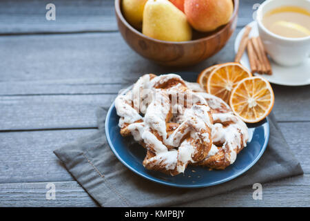 Bayerische Creme puff mit zerquetschten Haselnuss und Zitrone Fondant auf einem blauen Schild. Im Hintergrund, grüner Tee mit Zimtstangen und eine hölzerne Schüssel mit Stockfoto