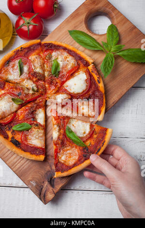 Nahaufnahme der köstliche italienische Pizza Margherita auf einem weißen Holztisch. Ansicht von oben. Woman's Hand nimmt ein Stück Pizza. Stockfoto