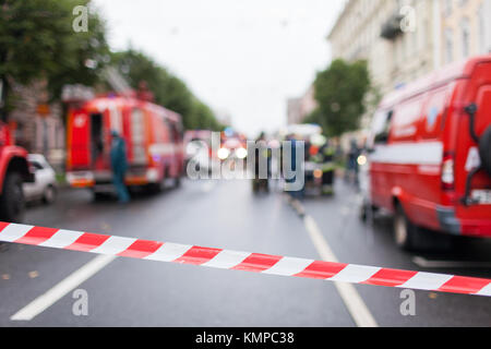 Rote und weiße Linien der Absperrband auf dem Hintergrund der Feuerwehrleute und Feuerwehrautos bei der Arbeit. Rot Weiß Warnband pole Fechten ist schützt für Nr. Stockfoto