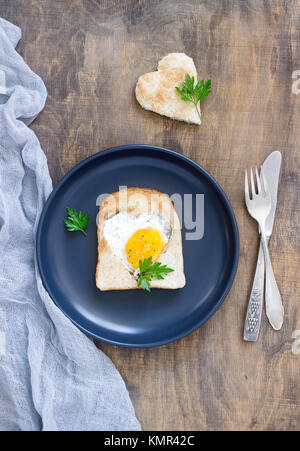 Ei in einen herzförmigen Brot mit Petersilie, romantisches Frühstück. Selektive konzentrieren. Stockfoto