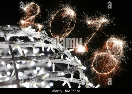 Isolierte 2018 Zeichen mit Schein Feuerwerk mit Weihnachtsbeleuchtung Dekoration auf dem schwarzen Hintergrund geschrieben, neues Jahr 2018 Konzept zufrieden. Stockfoto