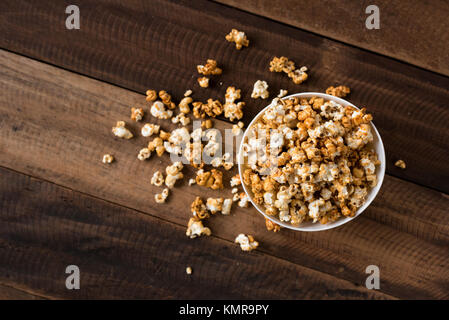Karamell Popcorn auf hölzernen Tisch Hintergrund. Karamell aromatisierter Popcorn in der Schüssel Stockfoto