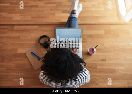 Hohen Winkel einer afrikanischen Frau Student online arbeiten mit einem Laptop beim Sitzen auf dem Boden in einem campus Flur zwischen Klassen trinken Stockfoto