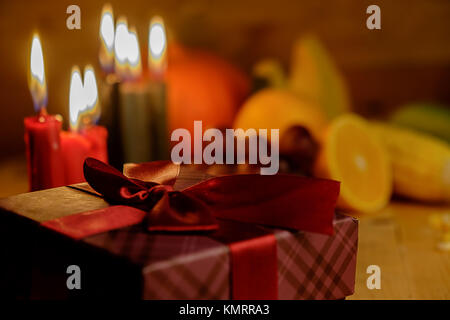 Kwanzaa urlaub Konzept mit sieben Kerzen Rot, Schwarz und Grün schmücken, Geschenkbox, Kürbis, Mais und Obst auf hölzernen Schreibtisch und Hintergrund. Stockfoto