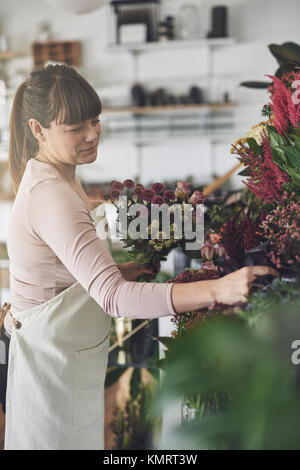 Lächelnde junge weibliche Blumengeschäft arbeitet sie in ihrem Blumenladen eine Vielzahl von Blumen auf einem Display Stockfoto