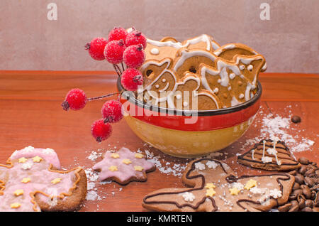 Eine Schüssel voll von Weihnachten Lebkuchen mit weißer Glasur, Kaffeebohnen und Rowan Zweig für die Dekoration auf einem Holzbrett Stockfoto