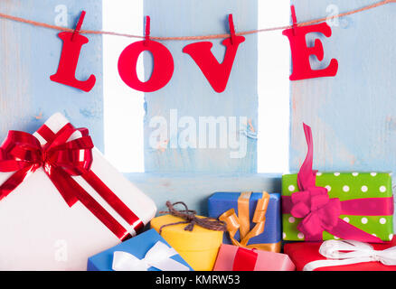 Liebe aus rotem Papier geschrieben und in einen String mit Holz- Clips gebunden, auf blauem Holzzaun und einer Fülle von Cognac Geschenkverpackungen. Stockfoto