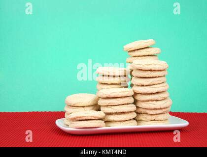 Sugar Cookies auf mehreren Höhen auf einem weißen rechteckigen Platte rot Tischset, grün Hintergrund gestapelt. Stockfoto