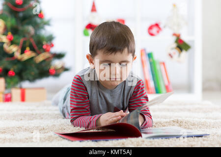 Niedliche Kind Junge mit einem Buch vor dem Weihnachtsbaum, Weihnachten Stockfoto