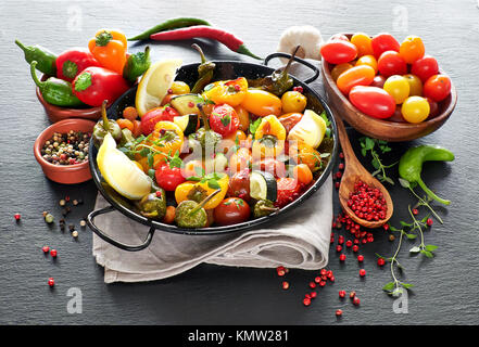 Rustikal, Ofen gebackenes Gemüse mit Gewürzen und Kräutern in Runde Metall Backform. Saisonale vegetarische vegane Mahlzeit auf dunklem Stein. Zutaten: Zucchini, t Stockfoto