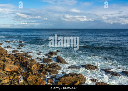 Küste mit Felsen, Wellen krochen vorsichtig Tonto die Felsen der Küste bilden keine weißen Schaum, tief blauen Wasser und blauen Himmel über mit flauschigen weißen cl Stockfoto