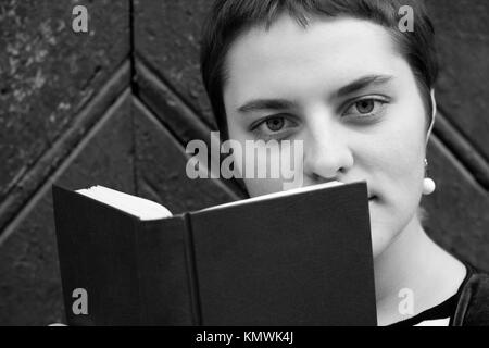 Ein Mädchen mit großen Augen und kurzes Haar versteckt sich hinter einem Buch. Close-up Portrait. Schwarz-weiß Foto. Stockfoto