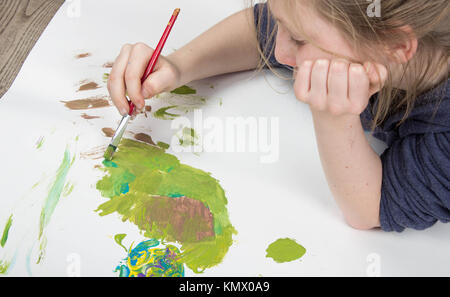 Junge Kind spielt mit Pinsel im splattered Farbe auf weißem Hintergrund Stockfoto