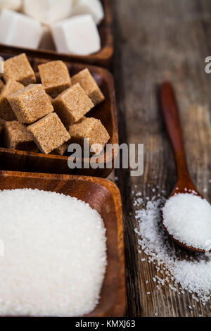 Drei Schalen mit Zucker und einem Löffel aus Holz auf einem alten Holz- Hintergrund. Stockfoto