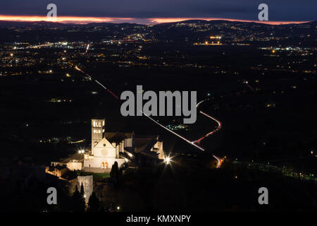 Luftaufnahme des hl. Franziskus in Assisi päpstliche Kirche bei Nacht, mit den Lichtern der Stadt füllen das Tal und weit entfernten dunklen Farben im Himmel Stockfoto