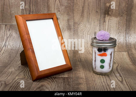 Hintergrund der leeren Holz Bilderrahmen Einstellung einem Holzregal mit einer Hand gestaltete Schneemann mit Zweigen, Tasten und Baumwolle Bälle in einem jar. Stockfoto