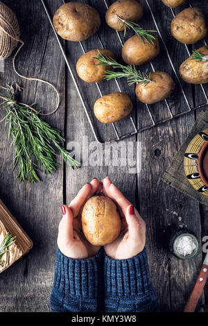 Kochen Frau Kartoffeln mit Rosmarin auf rustikalen Holzmöbeln Hintergrund in der Küche Stockfoto
