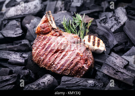 Gegrilltes Steak mit Knoblauch und Rosmarin auf schwarze Kohlen im Grill cookout Stockfoto