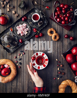 Frau berühren roter Tee in der Nähe der türkischen Köstlichkeiten rahat Lokum, simits und Früchte auf hölzernen Tisch Stockfoto