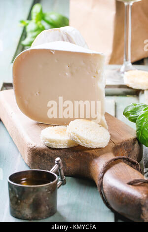 Ziegenkäse, serviert mit frischem Basilikum und Brot auf Holzbrett über Türkis Holztisch. Stockfoto