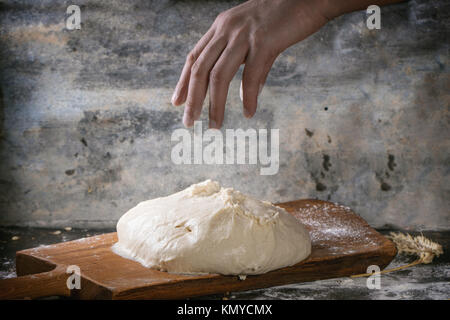 Hand des Mannes in Pulverform mit Mehl den Teig für Pizza auf Holzbrett über dunkle Küchentisch Stockfoto