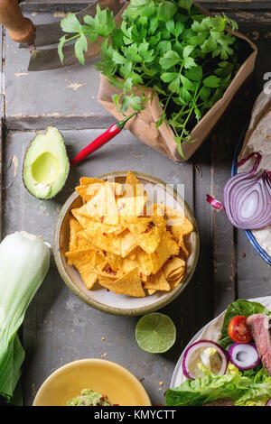 Draufsicht auf mexikanischen Stil Abendessen mit Gemüse, Tacos, Nachos Chips und Guakomole, serviert auf grauem Holztisch. Stockfoto