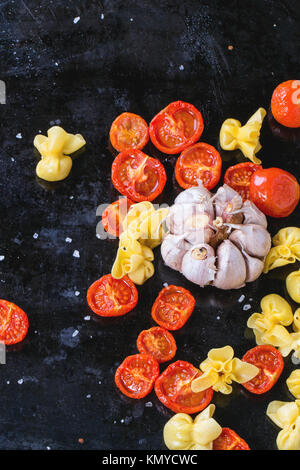 Nudeln Sacchettini und Sonne getrocknet Cherry-Tomaten mit Knoblauch und Meer Salz über schwarze Metall-Backblech. Ansicht von oben Stockfoto