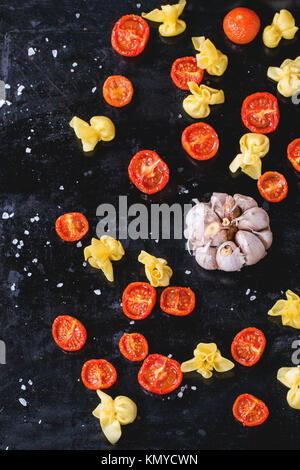 Nudeln Sacchettini und Sonne getrocknet Cherry-Tomaten mit Knoblauch und Meer Salz über schwarze Metall-Backblech. Ansicht von oben Stockfoto