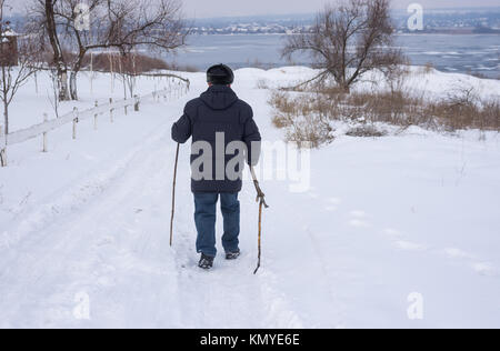 Reifer Mann zu Fuß auf einer verschneiten Straße hinunter nach gefrorenen Fluss Dnjepr in der Ukraine Stockfoto