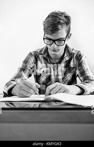 Der Student mit Brille Teenager ist eine Hausaufgabe, schreibt er in der Arbeitsmappe. Stockfoto