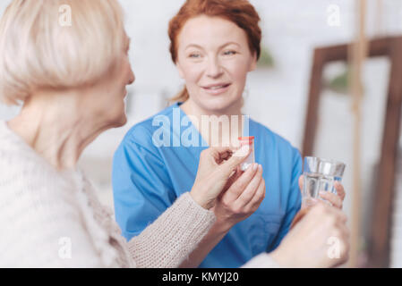 Fröhliche Krankenschwester, die Flasche mit Pille und Wasser zu Patient Stockfoto