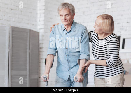 Ausschreibung ältere Dame kümmert sich um Mann auf Krücken Stockfoto