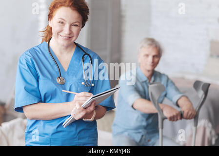 Positiv gesinnten medizinischer Arbeiter lächelnd, während die, die sich Notizen machen Stockfoto