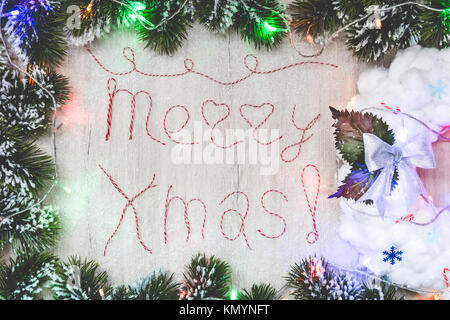 Die Worte "Merry Xmas" aus roten und weißen Faden Buchstaben auf Holz Textur mit Weihnachten Dekoration Stockfoto