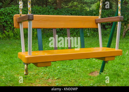 Kinder- Holz- Schwingen ist gelb auf die Seile. Der Sitz ist in der Nähe. Stockfoto