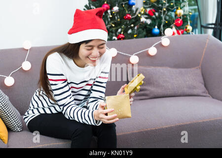 Asiatische Frau Auge wenn offen Gold xmas Geschenkverpackung im Holiday Party auf Sofa, überraschung Weihnachten Party vorhanden Stockfoto