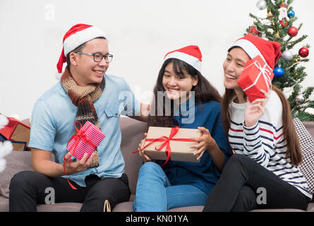 Gruppe von Asien Freunde sitzen auf einem Sofa feiern Weihnachten und Silvester Party mit Geschenk Austausch auf schmücken Baum, Geschenke urlaub Konzept. Glück Stockfoto