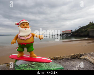 Surfen Santa auf der North Beach in Tenby Pembrokeshire mit der rnli Lifeboat Station im Hintergrund Stockfoto